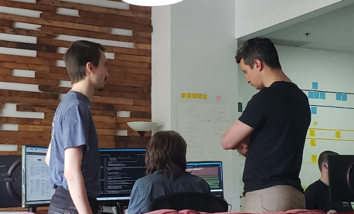 Three Moveck engineers talking through code and analysis plots at a standing desk in the Quebec City office